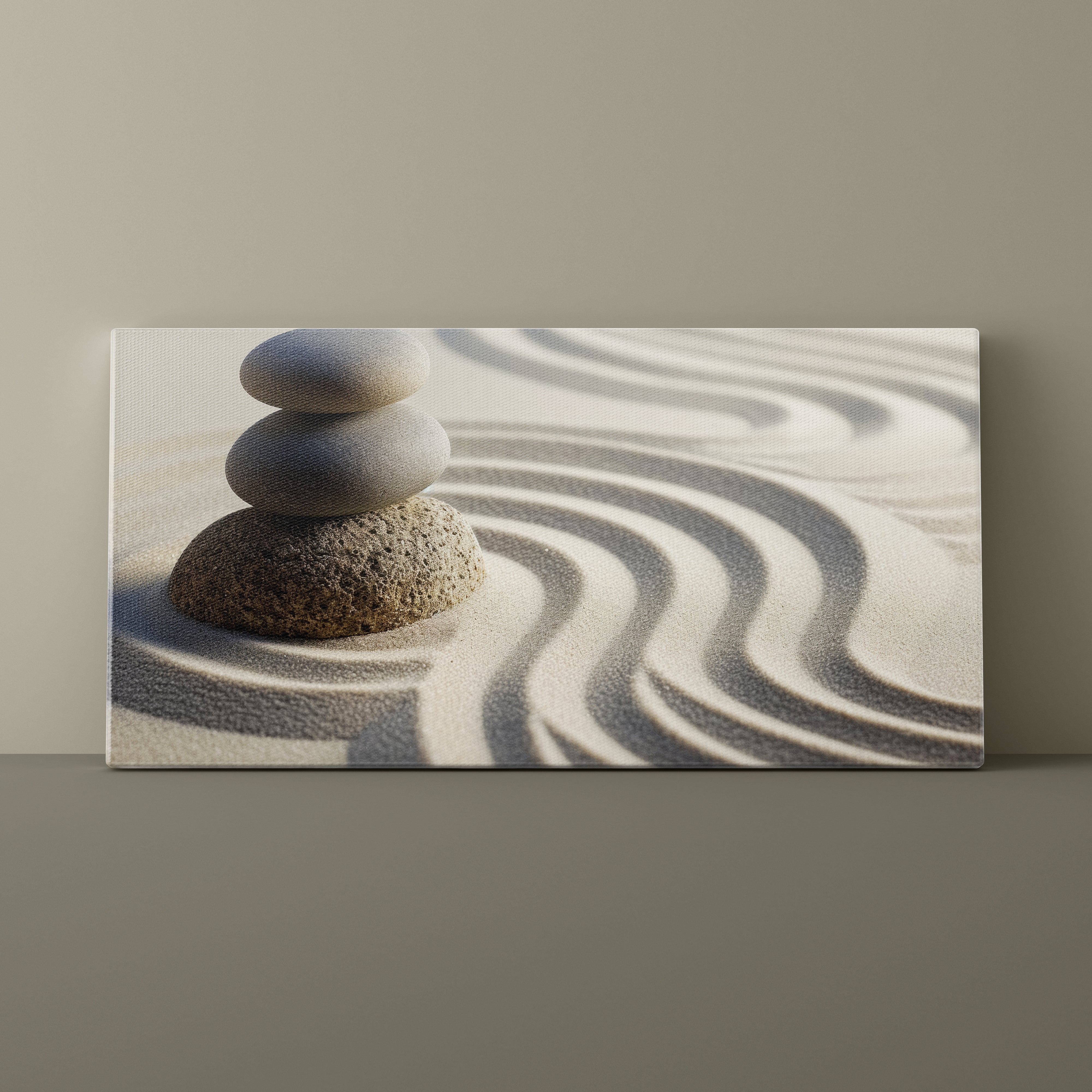 Canvas print of stacked stones on sand with wavy patterns, mounted on a beige wall.